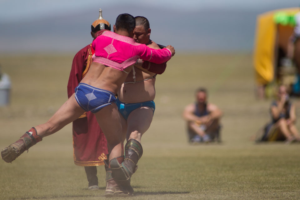 Two wrestlers battling it out at the Mongolian wrestling tournament at Kharkhorin Naadam. Standing behind keeping an eye on the match is a 'zasuul' or judge.